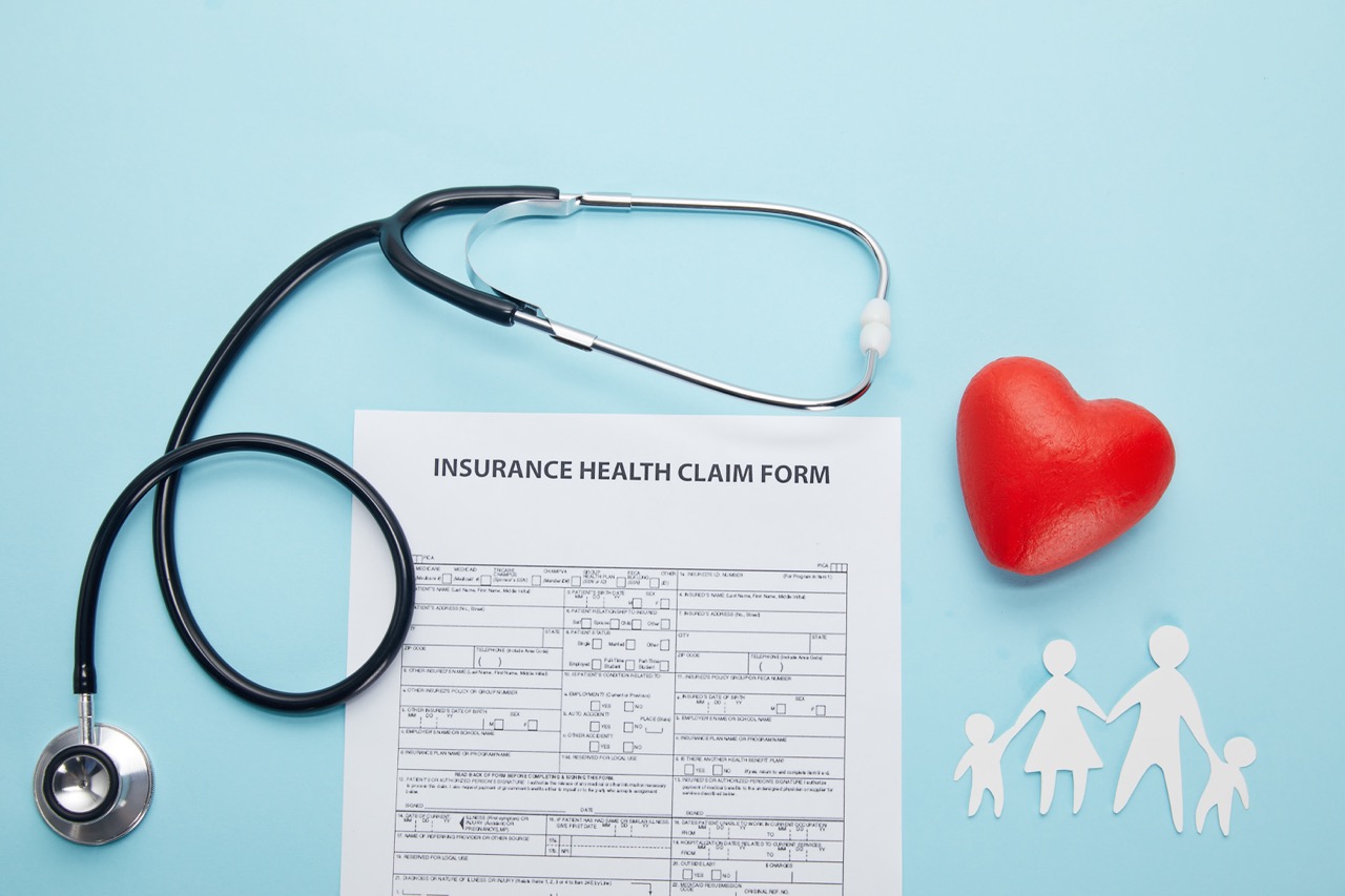New Patient 2 top view of insurance health claim form, paper cut family, red heart symbol and stethoscope on blue